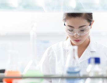 Medical lab technologist, seen from between shelves of beakers and vials