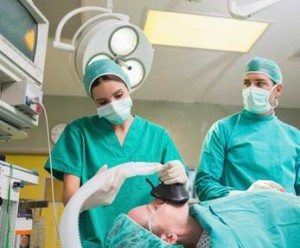 anesthesiologist, applies mask to patient as surgeon looks on