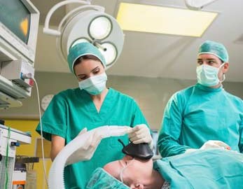 anesthesiologist, applies mask to patient as surgeon looks on