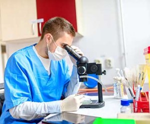 medical lab technician looks through microscope