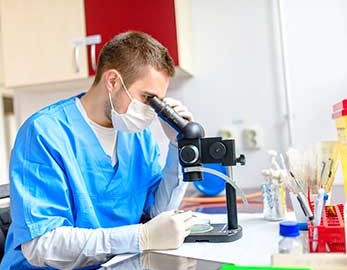 medical lab technician looks through microscope